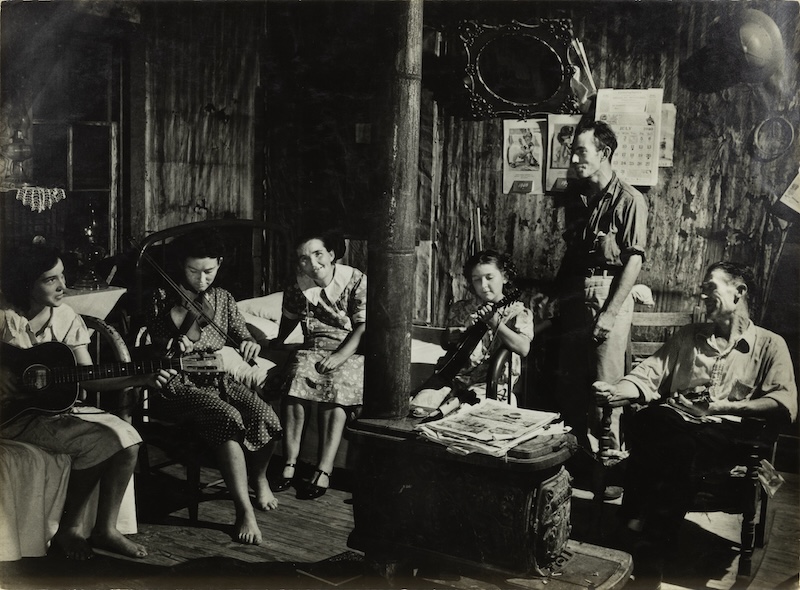 Sid Grossman's black-and-white photograph shows a family of folk musicians gathered around a wood-burning stove.
