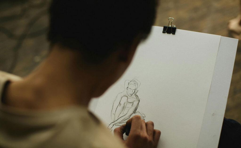 A stock photo image of a woman seen from behind, drawing a person on her sketchpad with a pencil