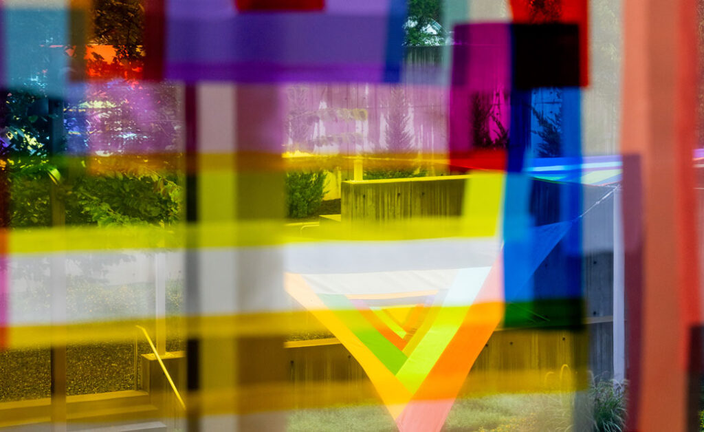 Color photograph of a Rachel Hayes textile sculpture installed in the museum's sculpture garden as seen through another Hayes textile sculpture installed inside on a window