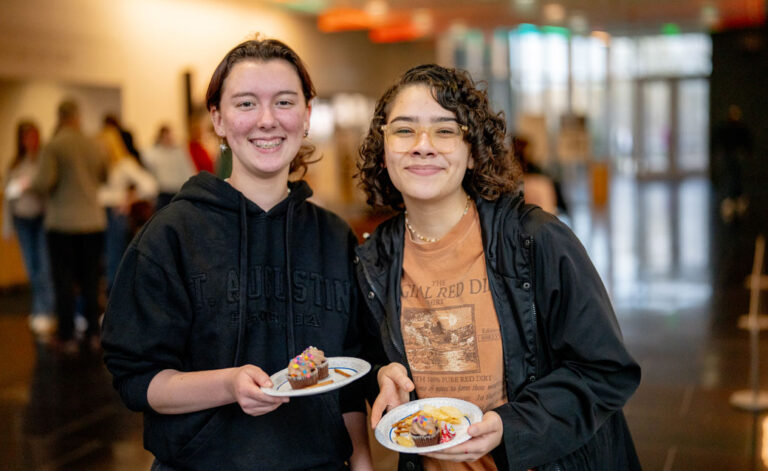 Two students at the February 2025 Student Night at the museum, holding plates with cupcakes on them