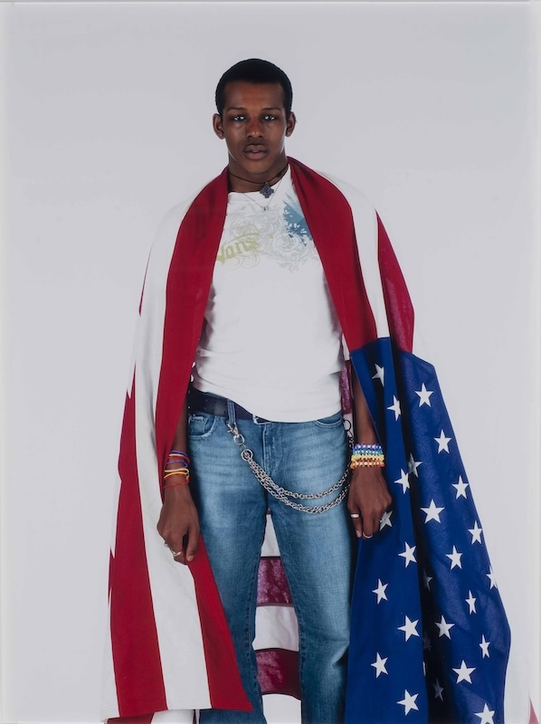 Sheila Pree bright's photograph, "Donovan," depicts a young Black man looking directly at the camera with an American flag draped across his shoulders