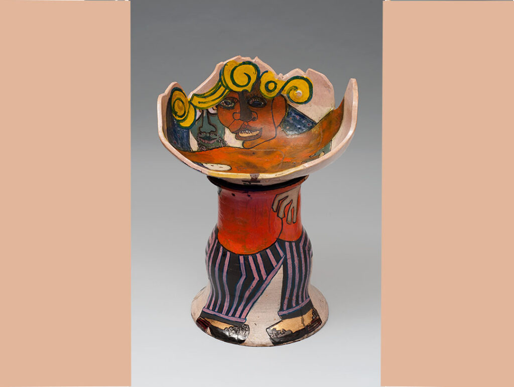 Camille Billops' Raku clay piece "El Pimpo's Chair," a stool with a half-sphere-shaped seat and a single large foot. The seat shows a topless Black woman, spreading out her arms. Behind her, embracing her, is a green-faced man, perhaps the pimp of the title. The painting/glazing continues on the rest of the stool, with the woman's legs and high-heel-shod feet pictured on the base and the man's purple-and-black-striped pants and his shoes.