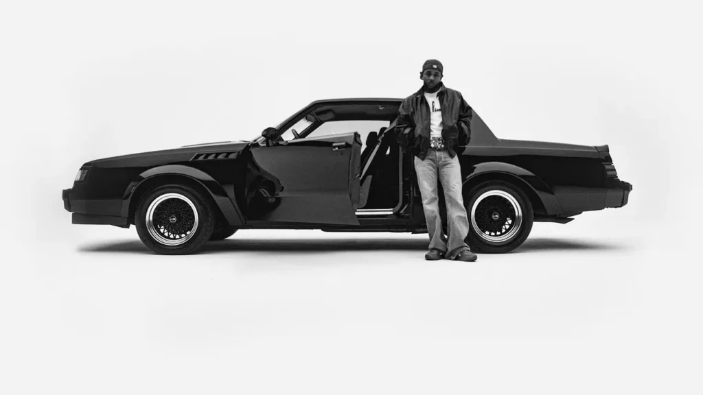 The cover image of Kendrick Lamar's album "GNX," featuring a black-and-white photo of Lamar standing in front of a Buick GNX