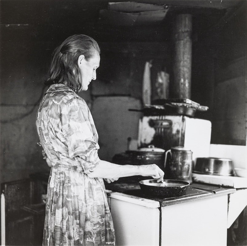 Arthur Tress' photograph depicts a woman preparing a meal over a wood-burning stove.
