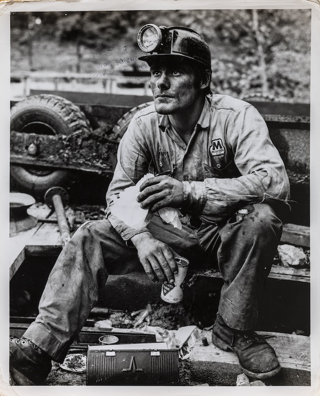 Arthur Tress' photograph "Deep Pit Coal Miner Eating Lunch" shows a coal miner holding a sandwich and can of cola.