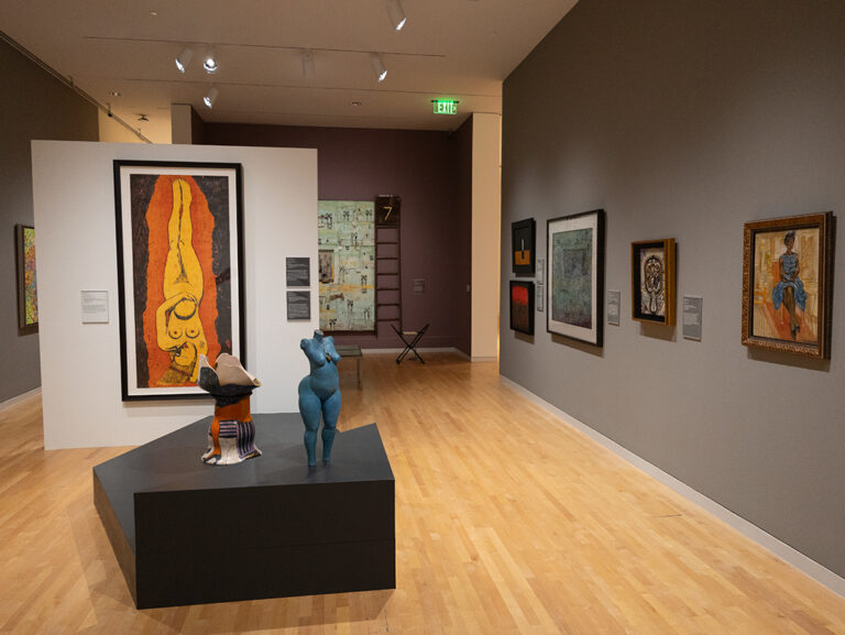 A view of the Larry D. and Brenda A Thompson Collection within the Boone and George-Ann Knox Gallery II. A variety of works hang on the wall, and two sculptures are on a platform in the center of the room.