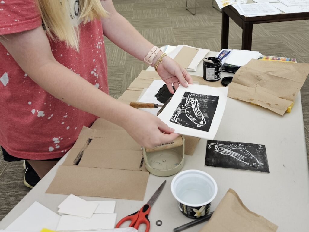 A person holds up a print of a bird at a table covered in crafting supplies.