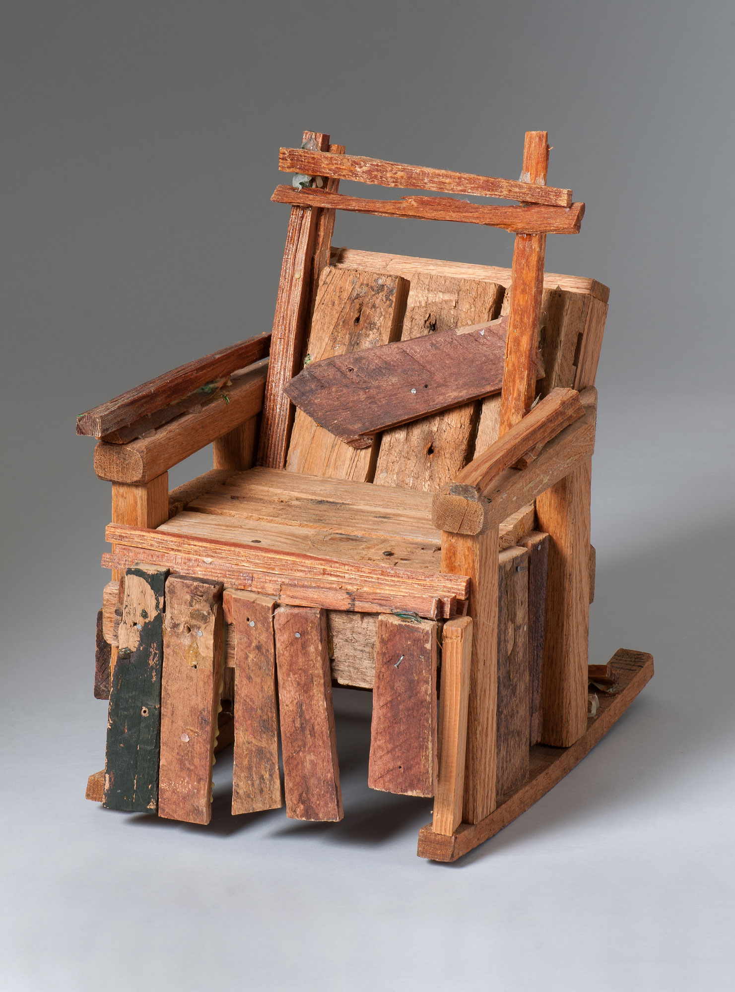 A tabletop sculpture by Beverly Buchanan titled "Bubba's Chair." Made of different sized pieces of wood, some of which have been colored on with ink, it looks rustic and handmade.