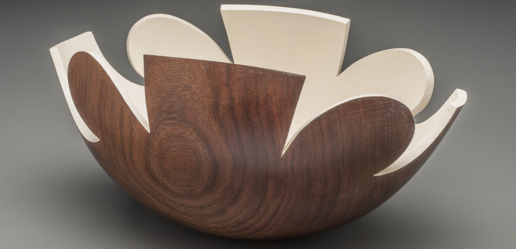 A photograph of a turned wood bowl that almost looks like a flower opening up. The outside features the wood grain, but the inside is white.
