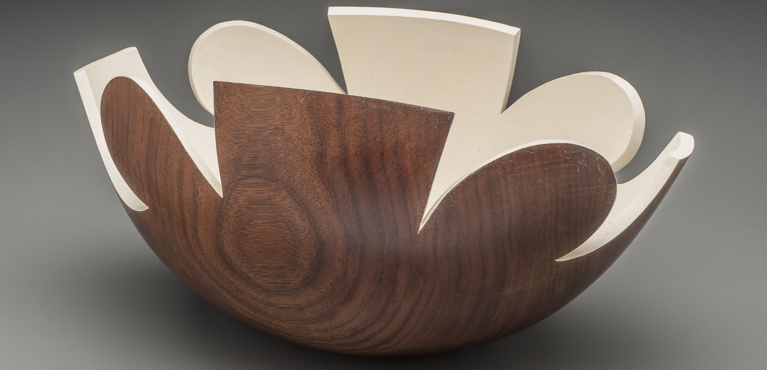 A photograph of a turned wood bowl that almost looks like a flower opening up. The outside features the wood grain, but the inside is white.