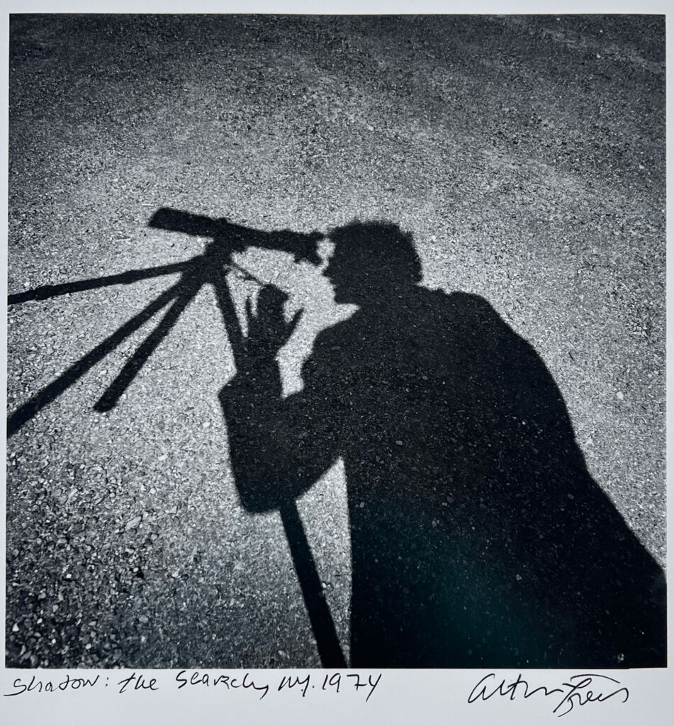 A black-and-white photograph by Arthur Tress that shows a shadow on the ground of a man looking through a telescope.