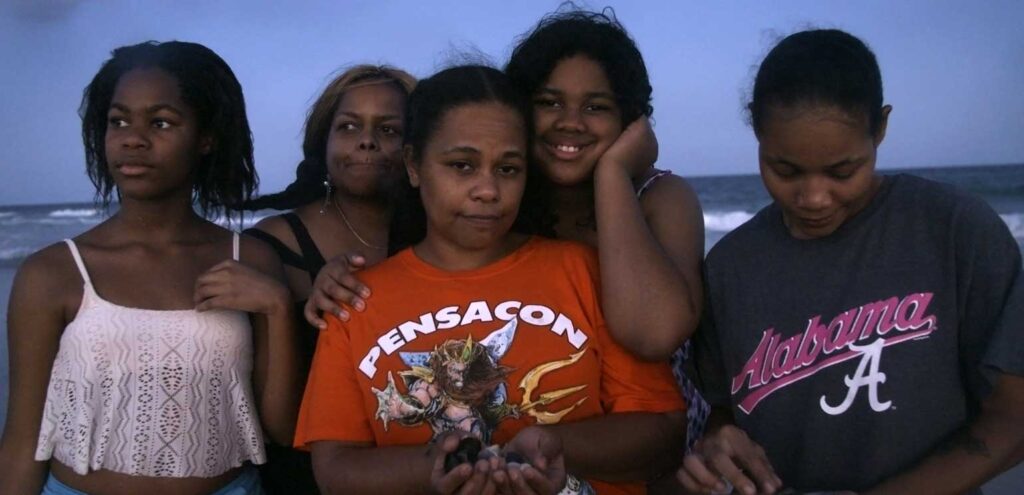 A still from Jennifer Crandall’s “Whitman, Alabama" that shows a Black family at the beach, clustered close together, their hair blowing in the wind.