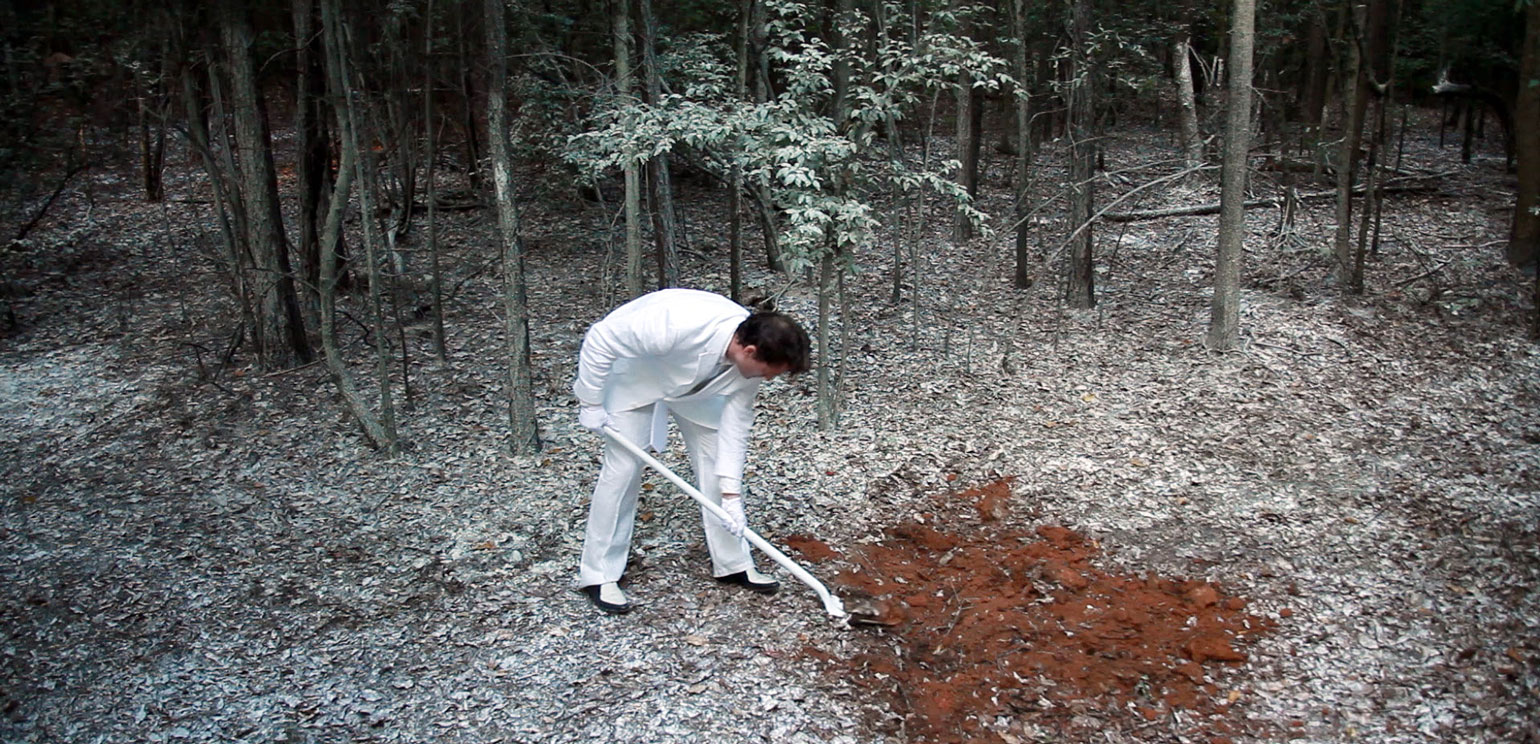 A detail of a still from a film by Adam Forrester, a graduating MFA candidate from the Lamar Dodd School of Art. Forrester appears in a white suite, using a white shovel to move red dirt.