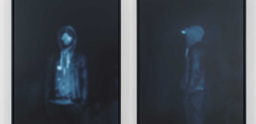 Two photographs by Carrie Mae Weems of young Black men, one seen facing forward, the other in profile. Their images are dark blue.