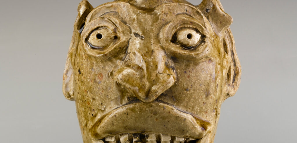 A close-up detail of a small face jug made in Edgefield, South Carolina