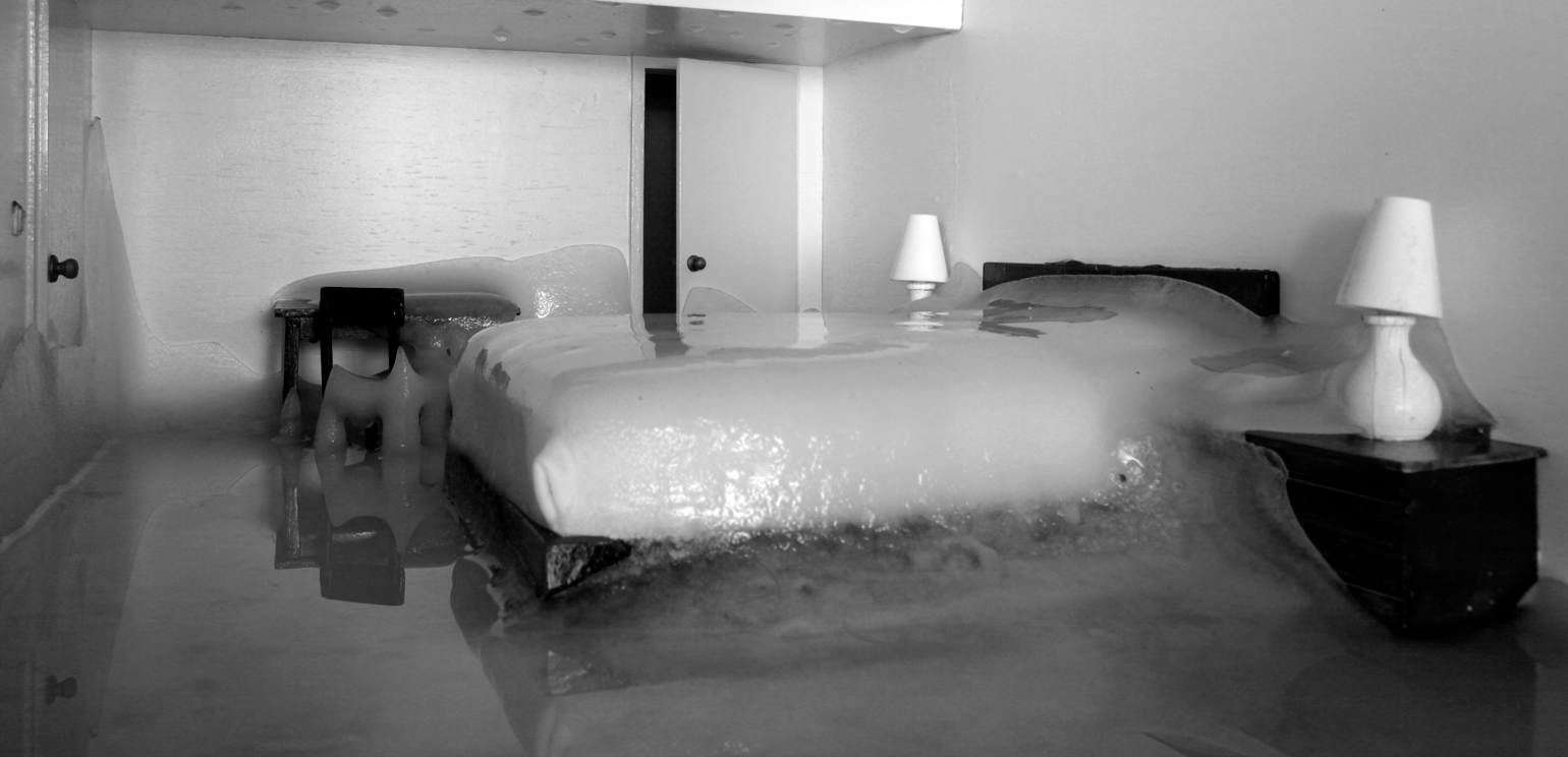 A detail of a still from Bernd Oppl's black-and-white film "Hotel Room," which looks like a bed, night tables, lamps, a desk and a chair encased in ice.