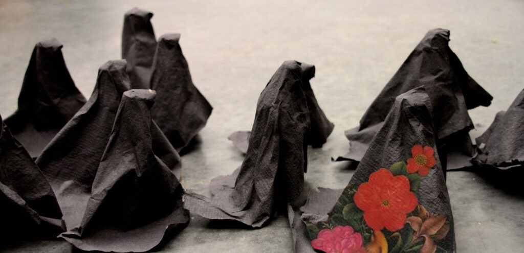 Detail of an installation piece by Sanaz Haghani that features a procession of tiny women (made of 3-D paper) wearing black burkas. One burka has hand-painted red flowers on it.