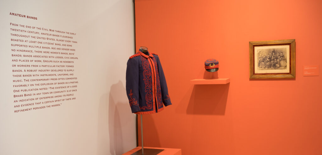 An installation photograph of the exhibition in the museum's galleries, including a band jacket, a hat and a print on the wall
