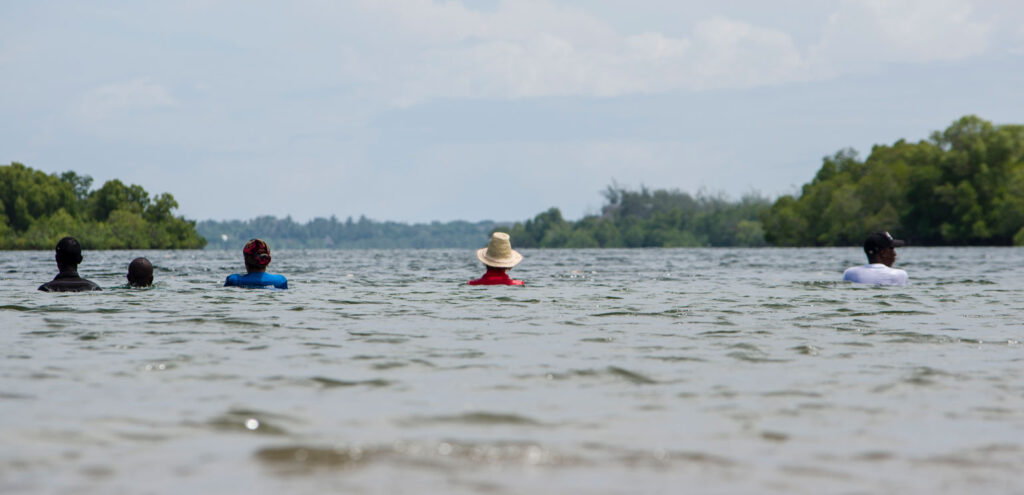 A photograph of Sarah Cameron Sunde performing her "36.5" series of performance art pieces in which she lets the tide almost cover here while she stands in the water for hours and hours, at Bodo Inlet, Kenya, in 2019.