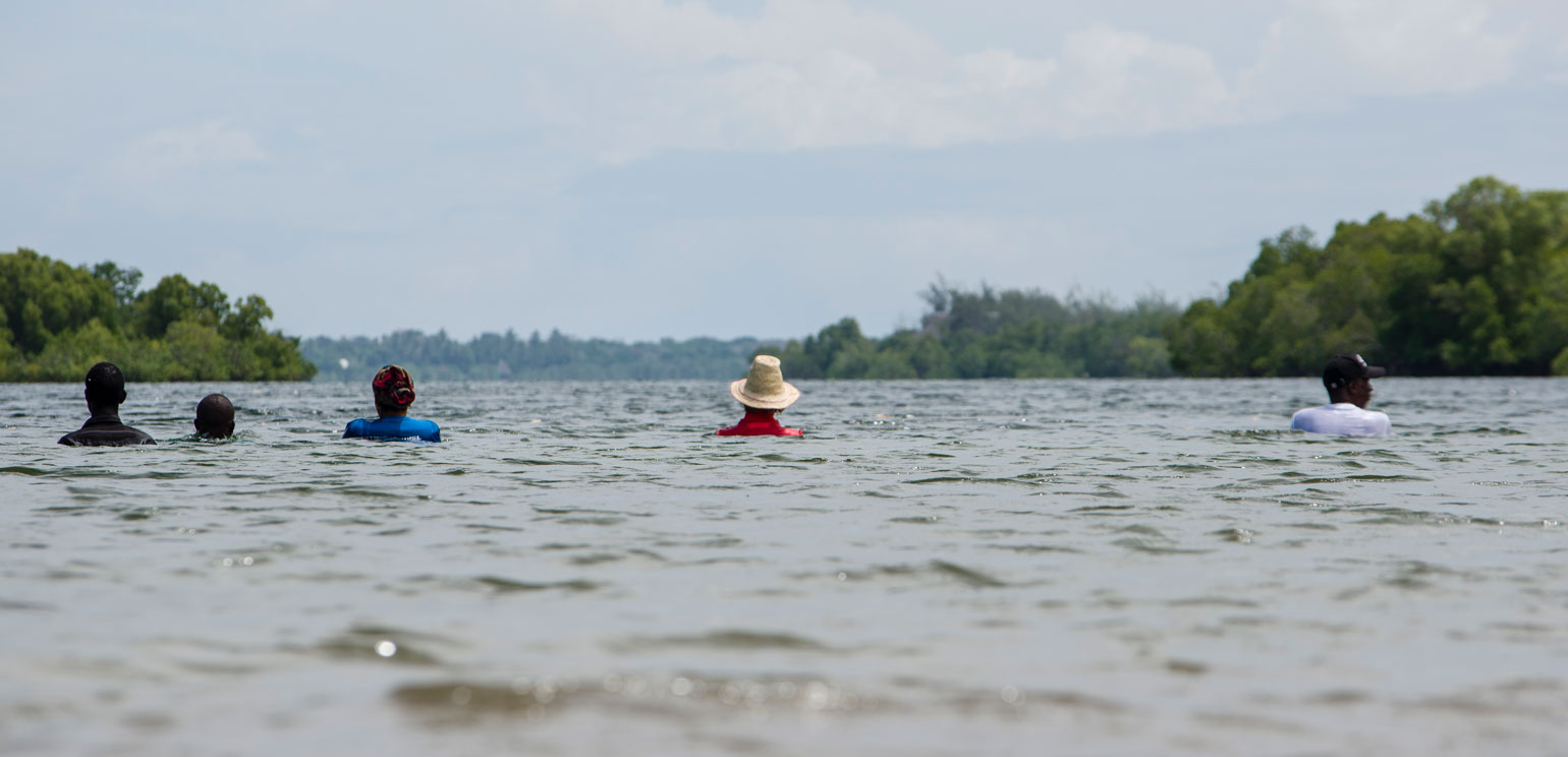 A photograph of Sarah Cameron Sunde performing her "36.5" series of performance art pieces in which she lets the tide almost cover here while she stands in the water for hours and hours, at Bodo Inlet, Kenya, in 2019.