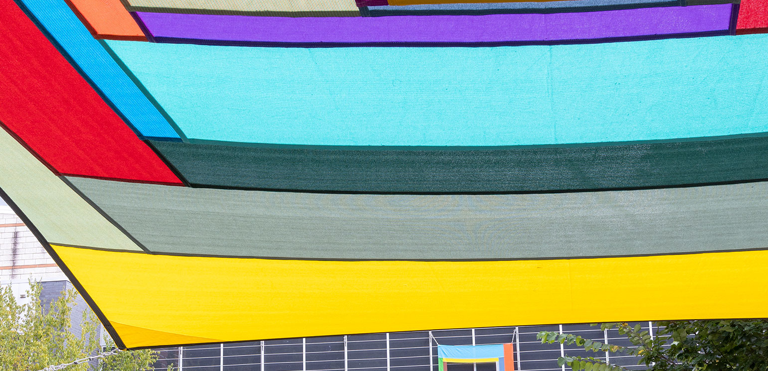 Colorful patchwork fabric hanging overhead with a glimpse of a building in the background