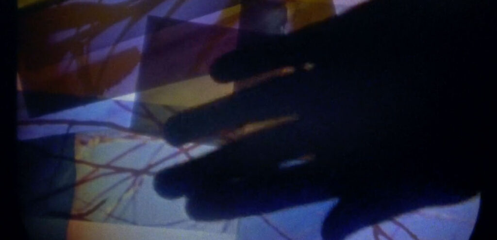 A detail of a screenshot from Sky Hopinka's film "Lore." It shows a silhouetted hand manipulating translucent blocks of color.