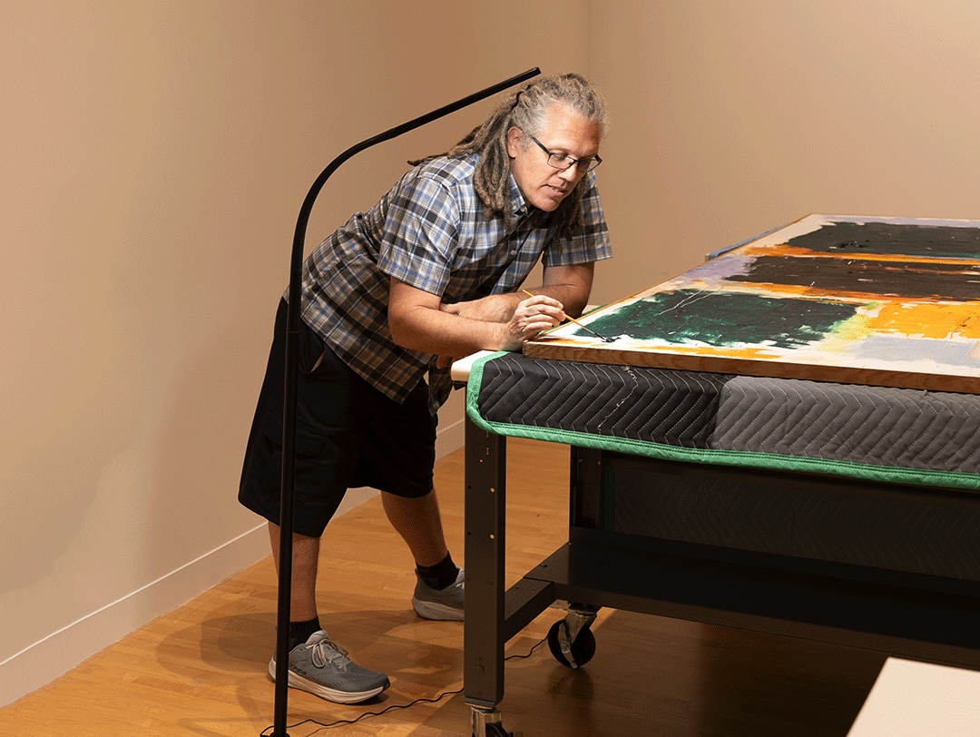 Art conservator Larry Shutts leans against a table while working on Joan Mitchell's painting, "Close."