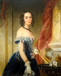 A portrait of Princess Elena Pavlovna Belosselsky-Belozersky by Christina Robertson. We see the princess' midsection. She wears a dark blue velvet gown overlaid with white lace and has a pale pink bow at her waist. She wears white gloves and holds a hand-painted, gold-trimmed fan in her left hand.