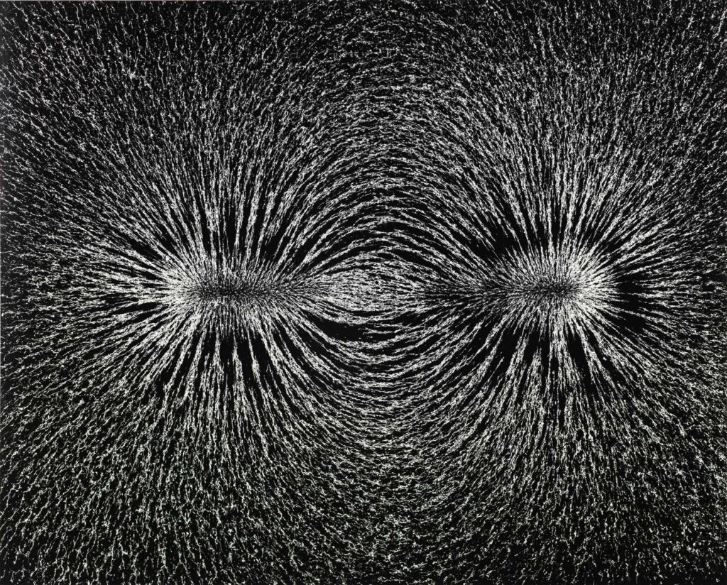 A black-and-white photograph by Berenice Abbott that shows metal filings attracted by a magnet, creating two starbursts of tiny white marks