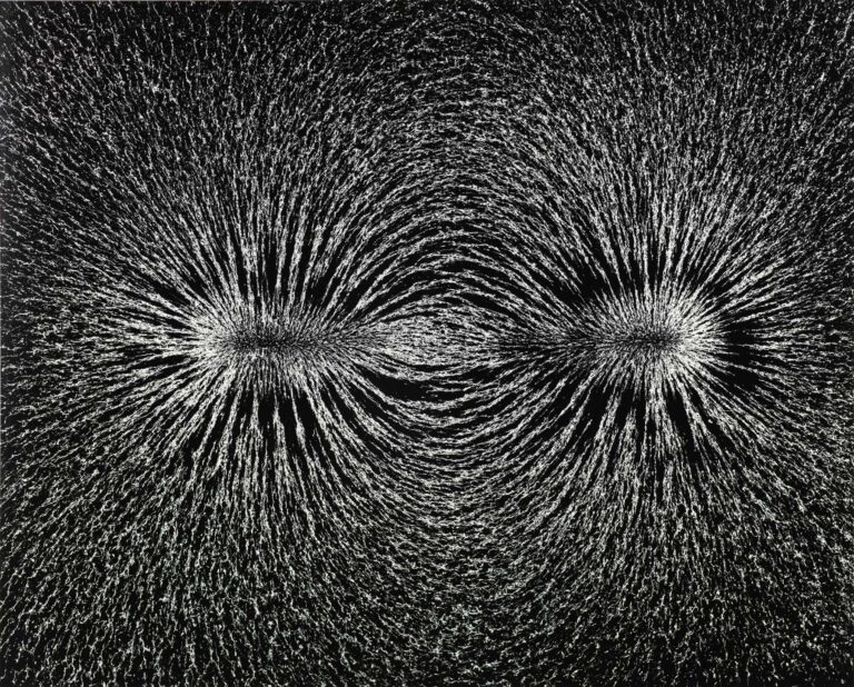 A black-and-white photograph by Berenice Abbott that shows metal filings attracted by a magnet, creating two starbursts of tiny white marks