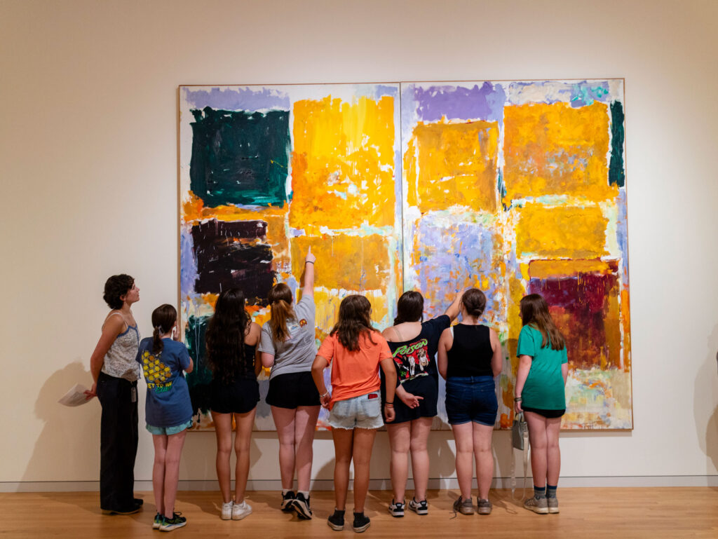 A group of young people on a visit to the museum, standing in front of a large abstract painting by Joan Mitchell, looking at it and pointing to different parts of it