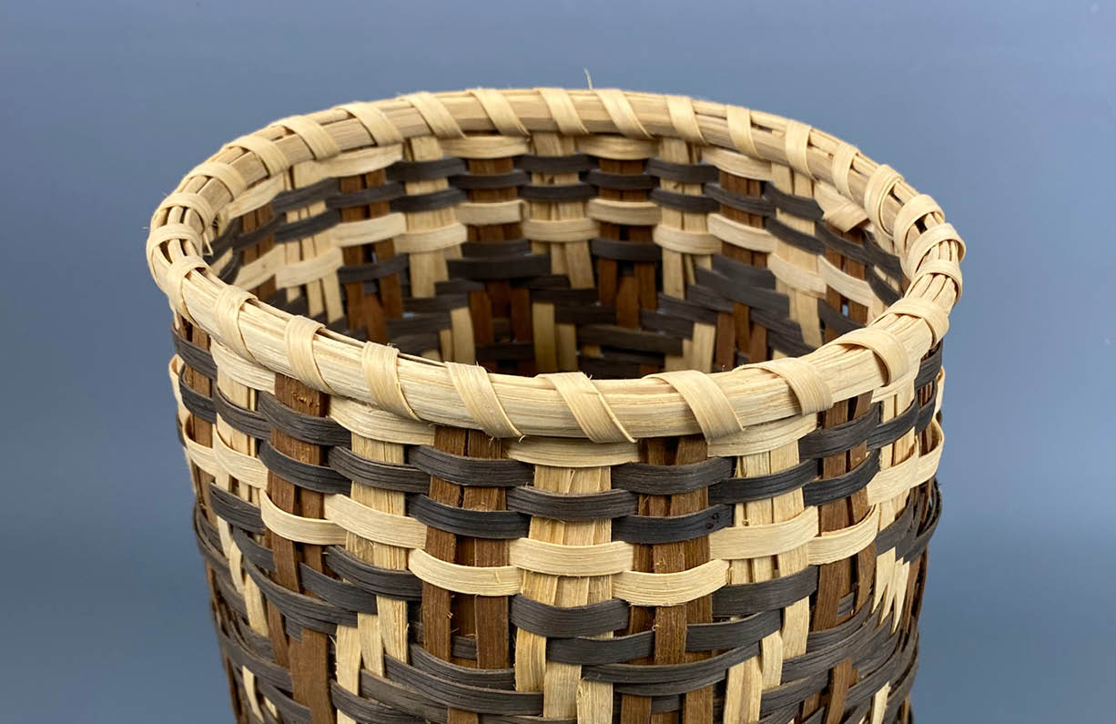 A Cherokee basket, woven with naturally dyed cane in brown and dark brown as well as pale brown.