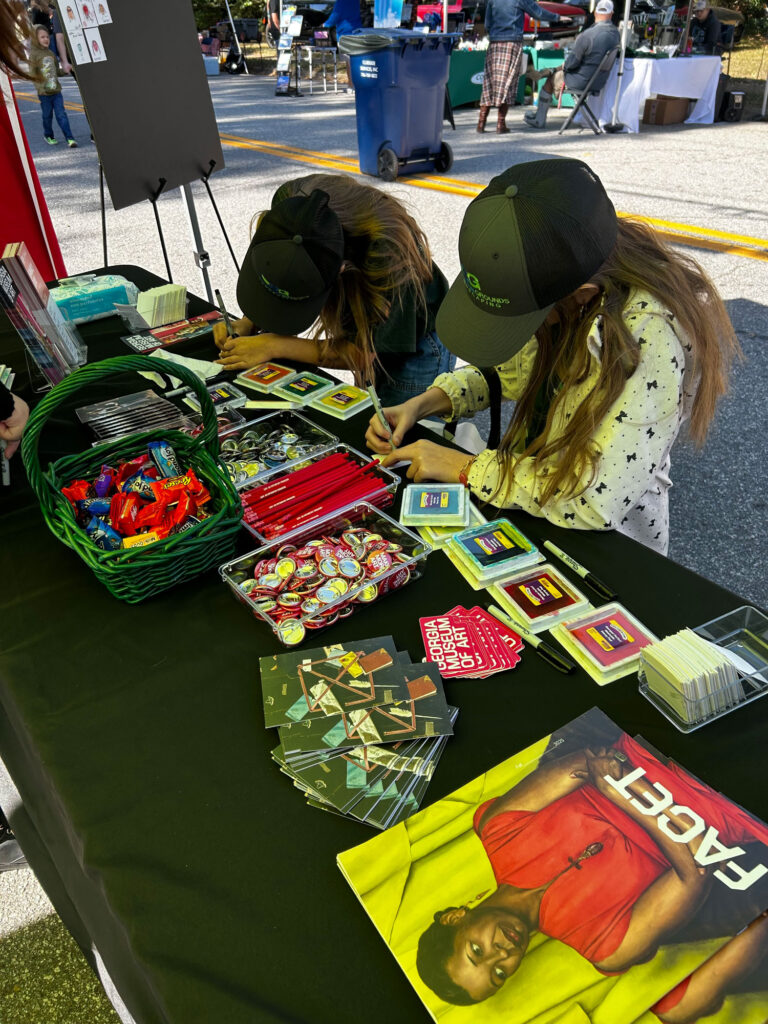 Two children participate in an art project at a table staffed by the museum