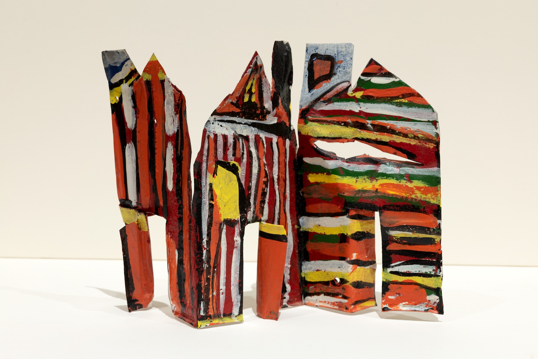 A metal house folded to stand upright with orange, yellow, white, green, red and black stripes