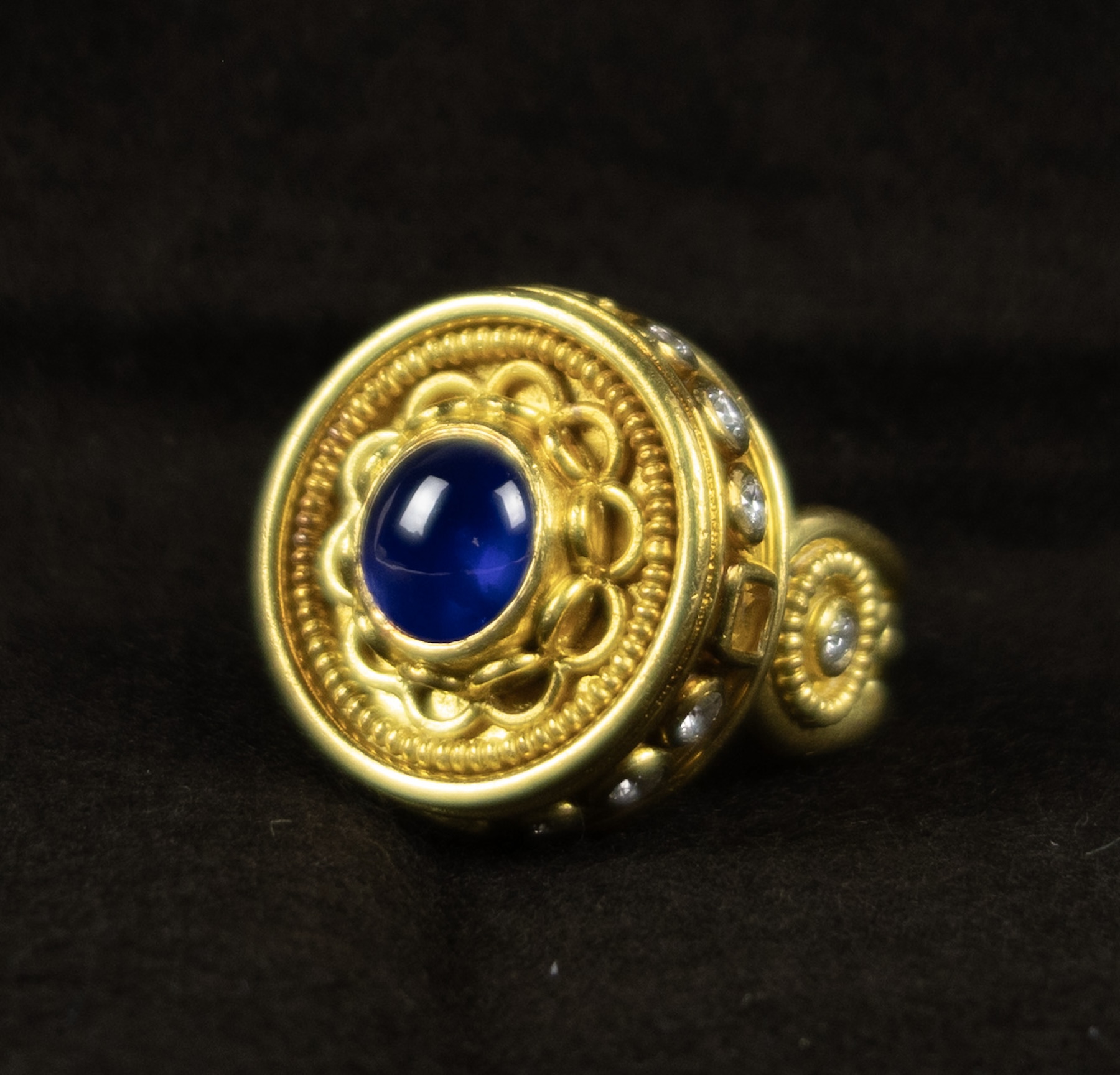 Gold ring with a blue cabochon saphhire in the center and row of small diamonds around the circumference