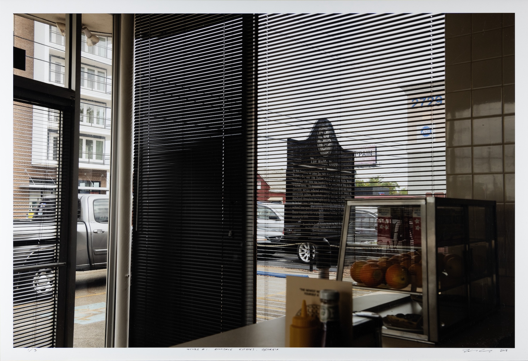 A photograph taken from behind the front counter of a Waffle House, looking through the blinds into the street