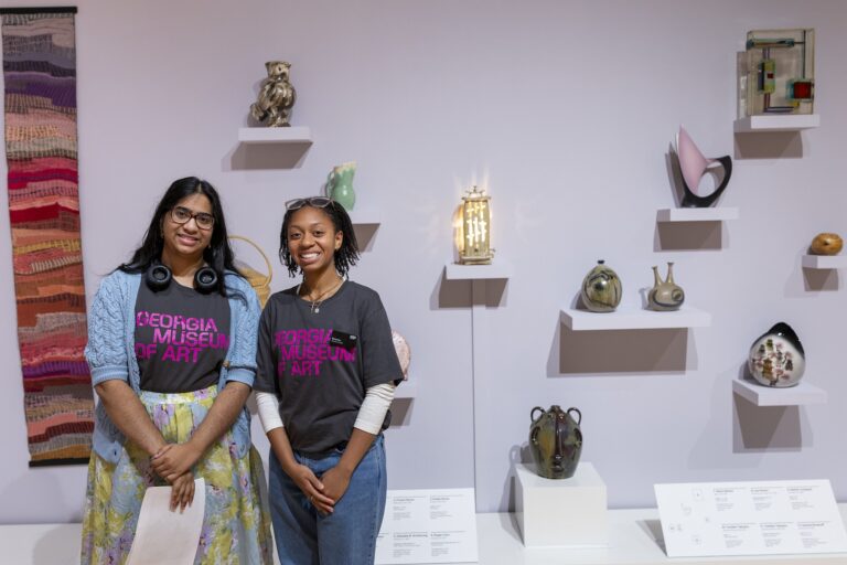 Two student guides standing in front of a wall displaying various objects