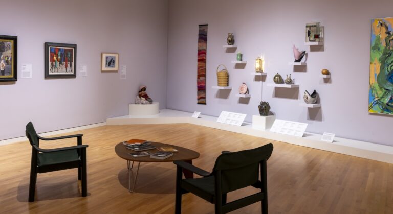 A pair of chairs face a wall of different objects in the Swanson Gallery