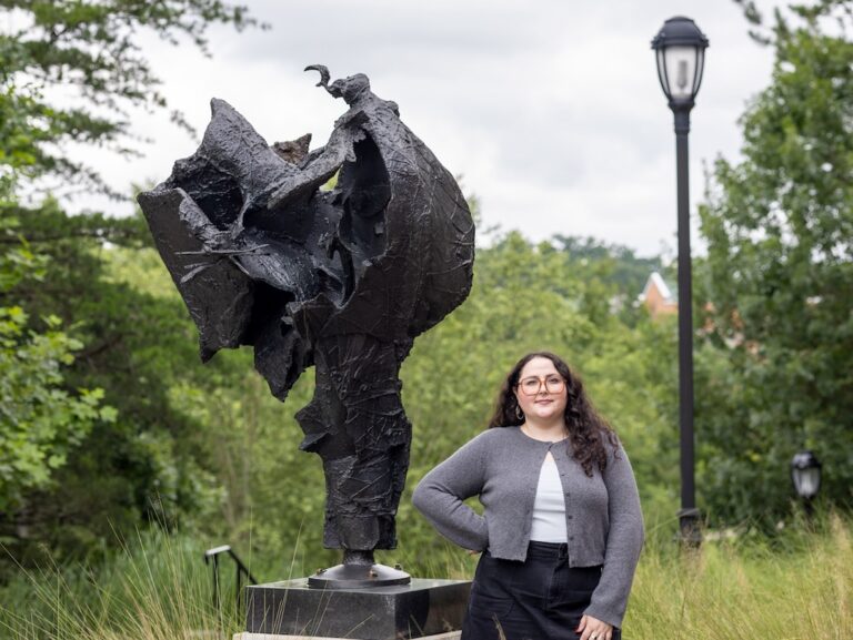 A portrait of William J. Thompson Curatorial Fellow Kelsey Siegert standing beside one of Thompson's sculptures