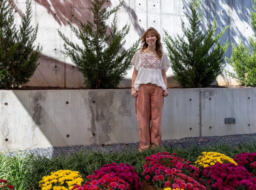 Museum programs assistant Ellen Patton stands near yellow and pink chrysanthemums in the museum's sculpture garden