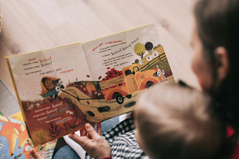 A stock photo of a woman reading a picture book to a child in her lap