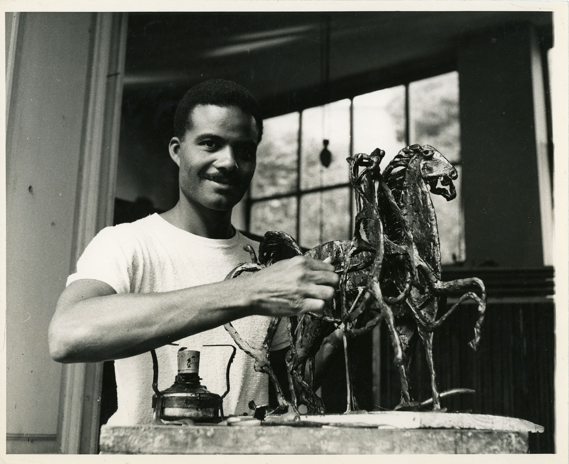 Black and white photograph of John Rhoden with his sculpture, "Three Horses."