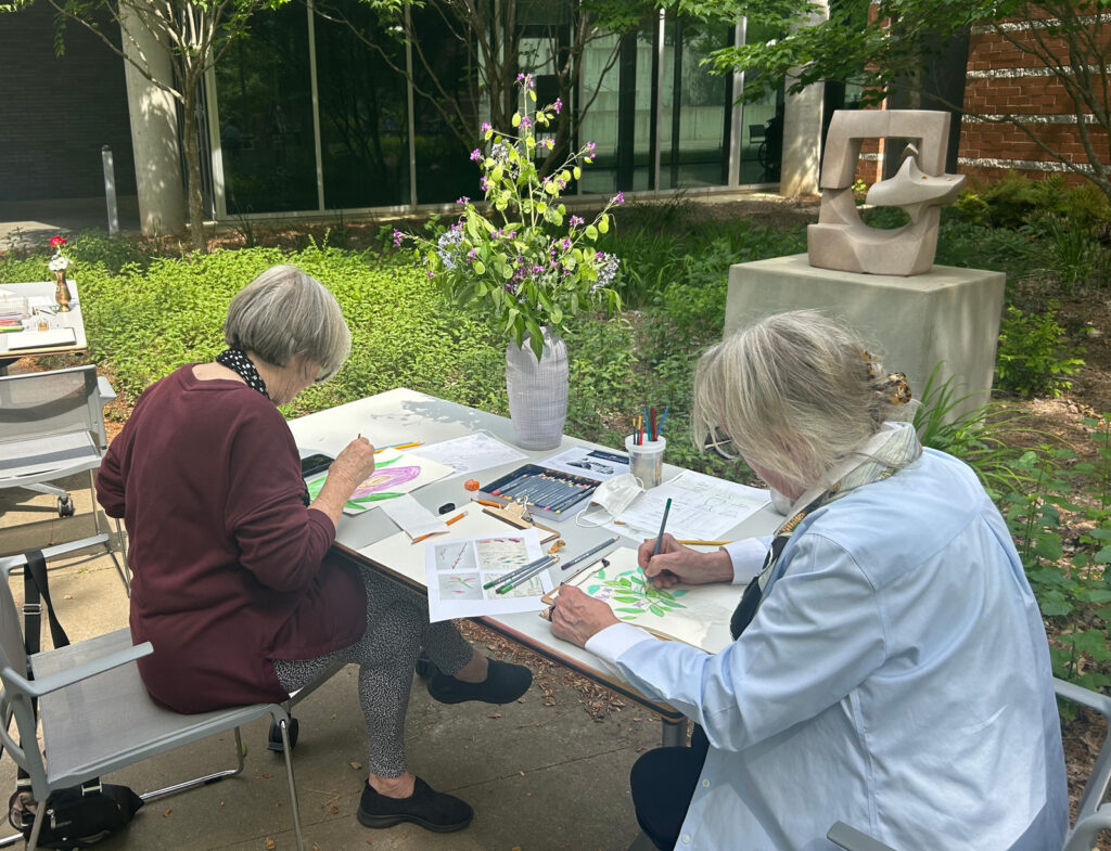 Two older women painting flowers outside