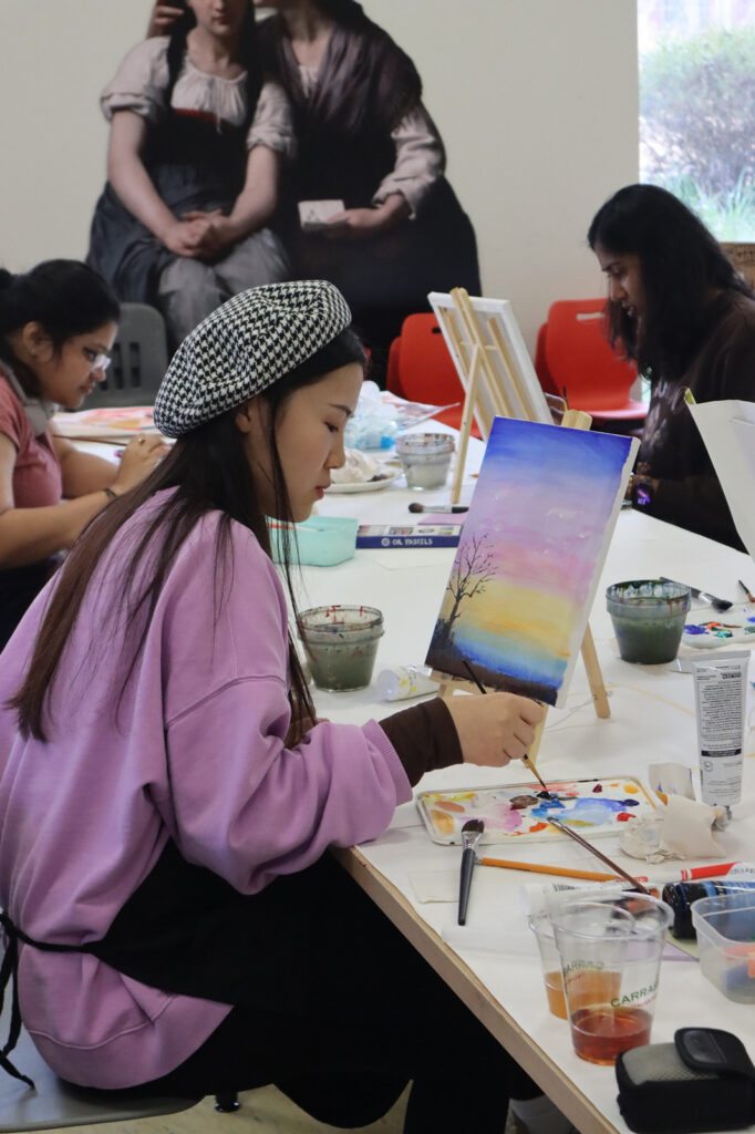 A UGA student in a beret painting a landscape in the museum's studio classroom
