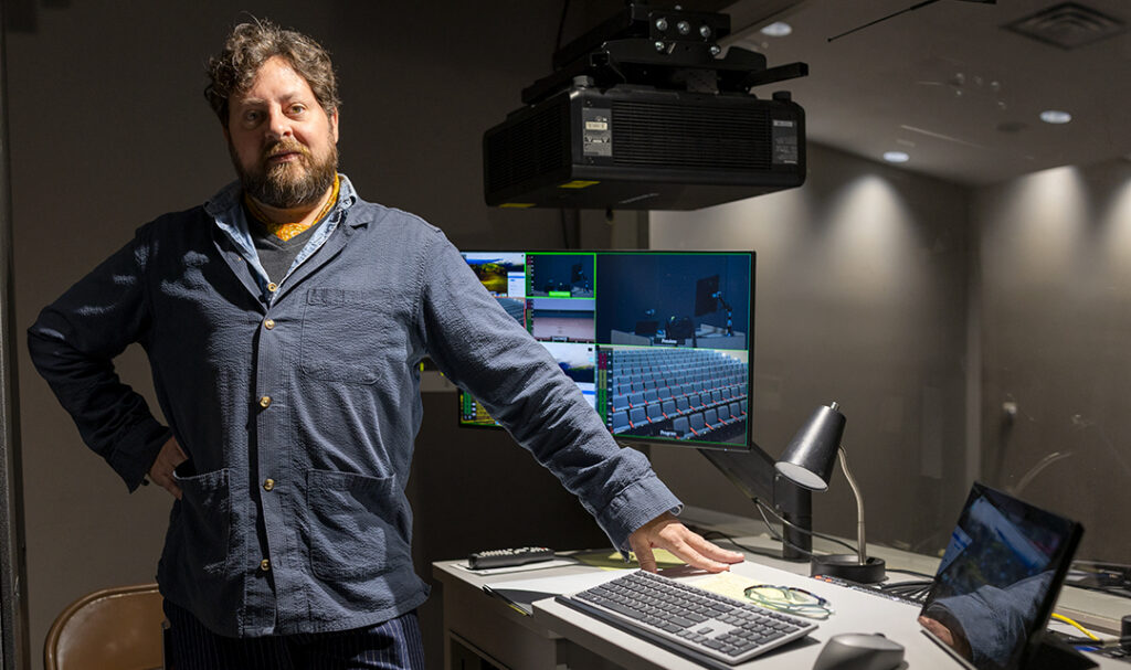 James Huggins, the museum's event technology specialist, stands next to a desk in the auditorium's control booth