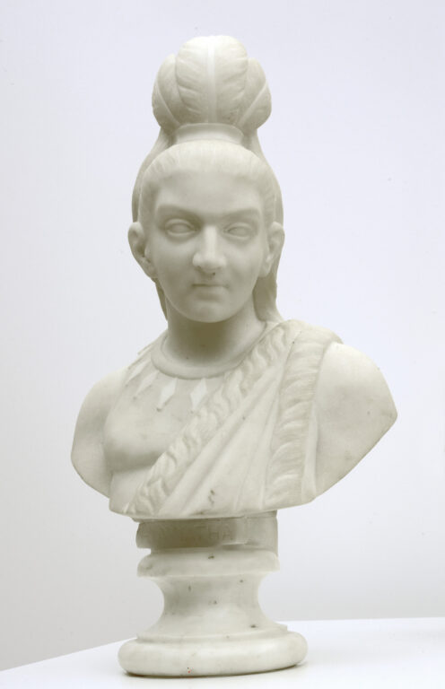 Edmonia Lewis’ small portrait bust of the character Hiawatha from Longfellow’s epic poem. He wears his hair in a topknot, with feathers, and has a necklace decorated with diamond shapes around his neck.