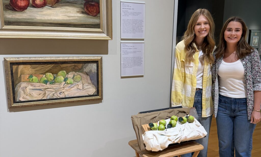 Two students stand next to a tactile image, or a three-dimensional model, of Pierre Daura's painting "Green Apples."