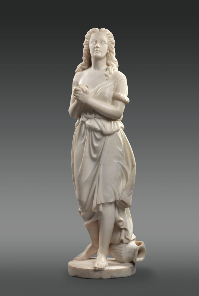 Edmonia Lewis’ marble sculpture of Hagar, the slave of the biblical Abraham and Sarah. She clasps her hands and looks up, her long hair flowing over her shoulders and her loose gown off her right shoulder. At her feet is an overturned water pitcher.