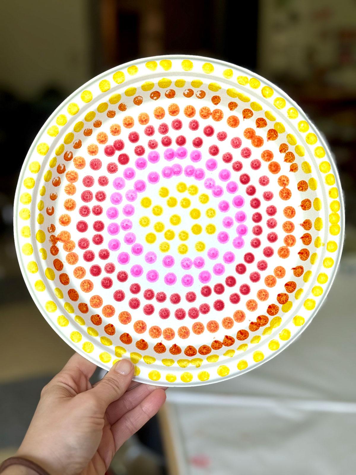 Paper plate with small, brightly-colored paint dots in a circular pattern.