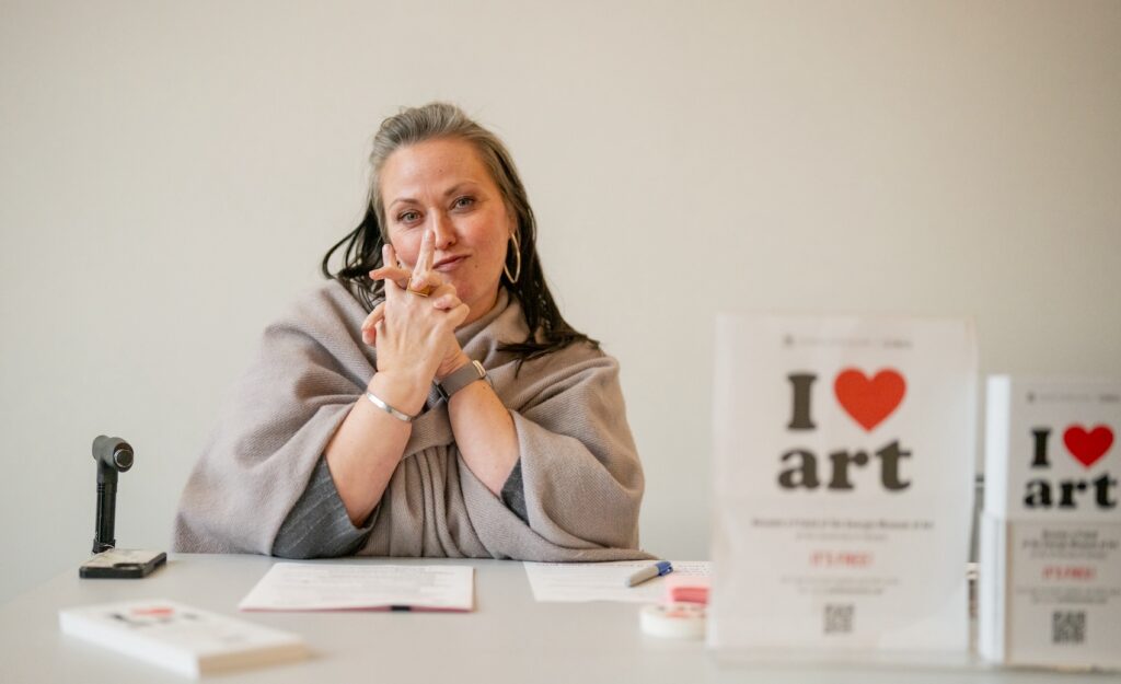 Michele Turner, director of annual giving and donor relations, sits at a table. On the table is a notepad and a display that says "I love art."